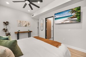 Un dormitorio con una cama, ventilador de techo, televisor y obras de arte en la pared.