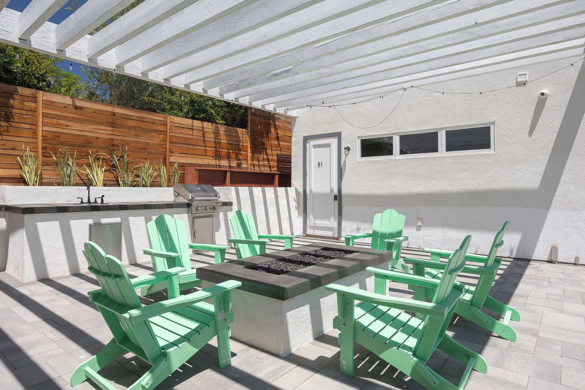 Eine Terrasse im Freien mit Feuerstelle, grünen Adirondack-Stühlen, Grill und Holzzaun.