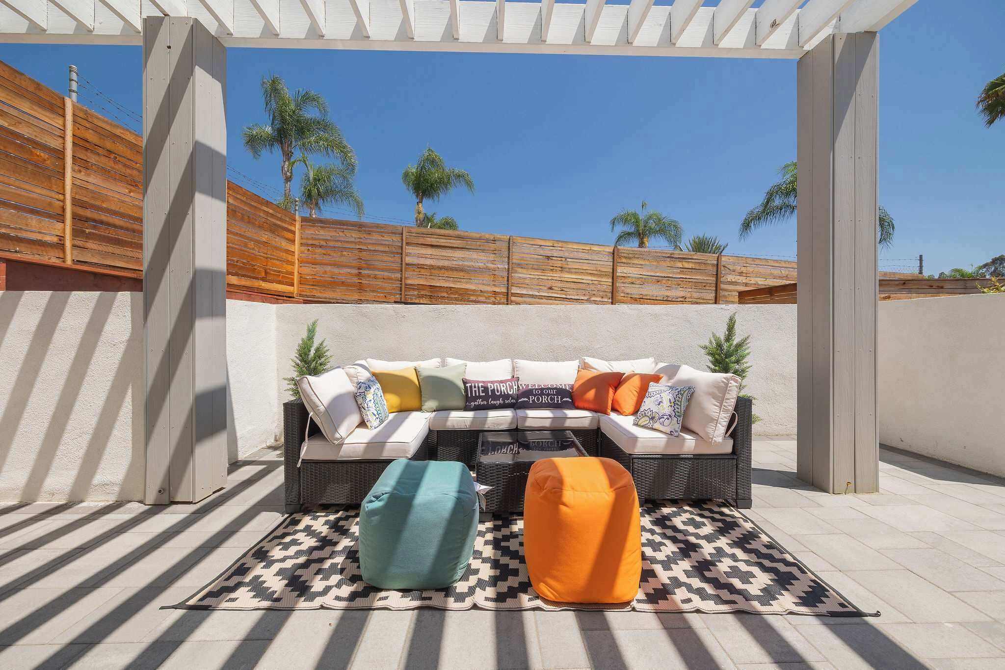 Un área de estar al aire libre con un sofá, dos sillones de tela y una alfombra estampada.