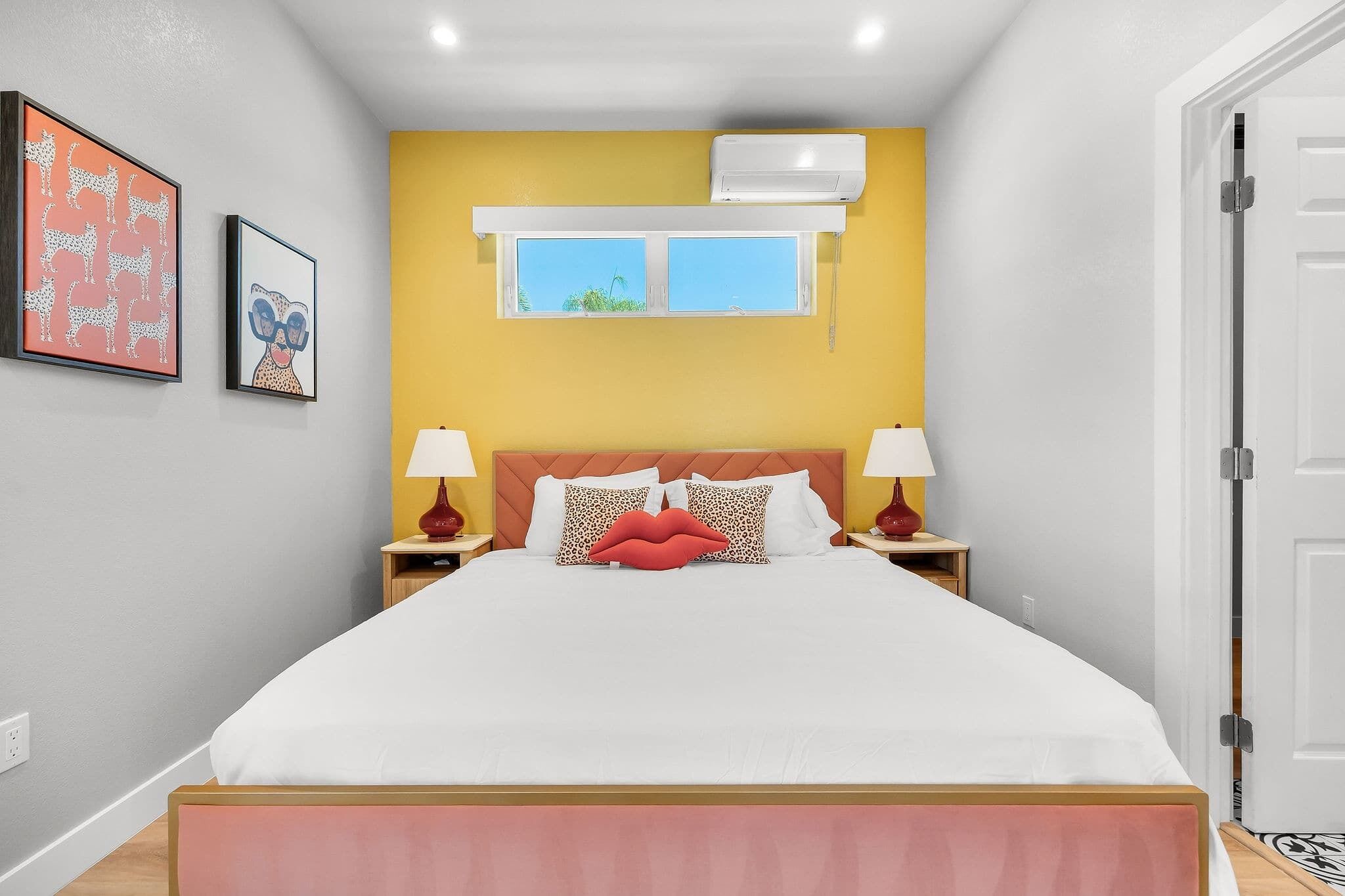 A bedroom with a bed, two nightstands, a window, and an air conditioning unit.