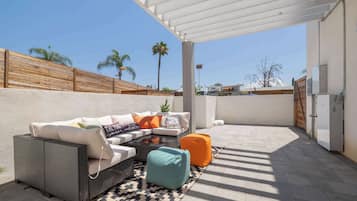 An outdoor patio with a wicker sofa, a patterned rug, and a wooden fence.