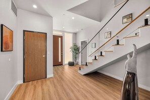 A modern interior with a wooden floor, a staircase with glass railings, and a door with a wooden finish.