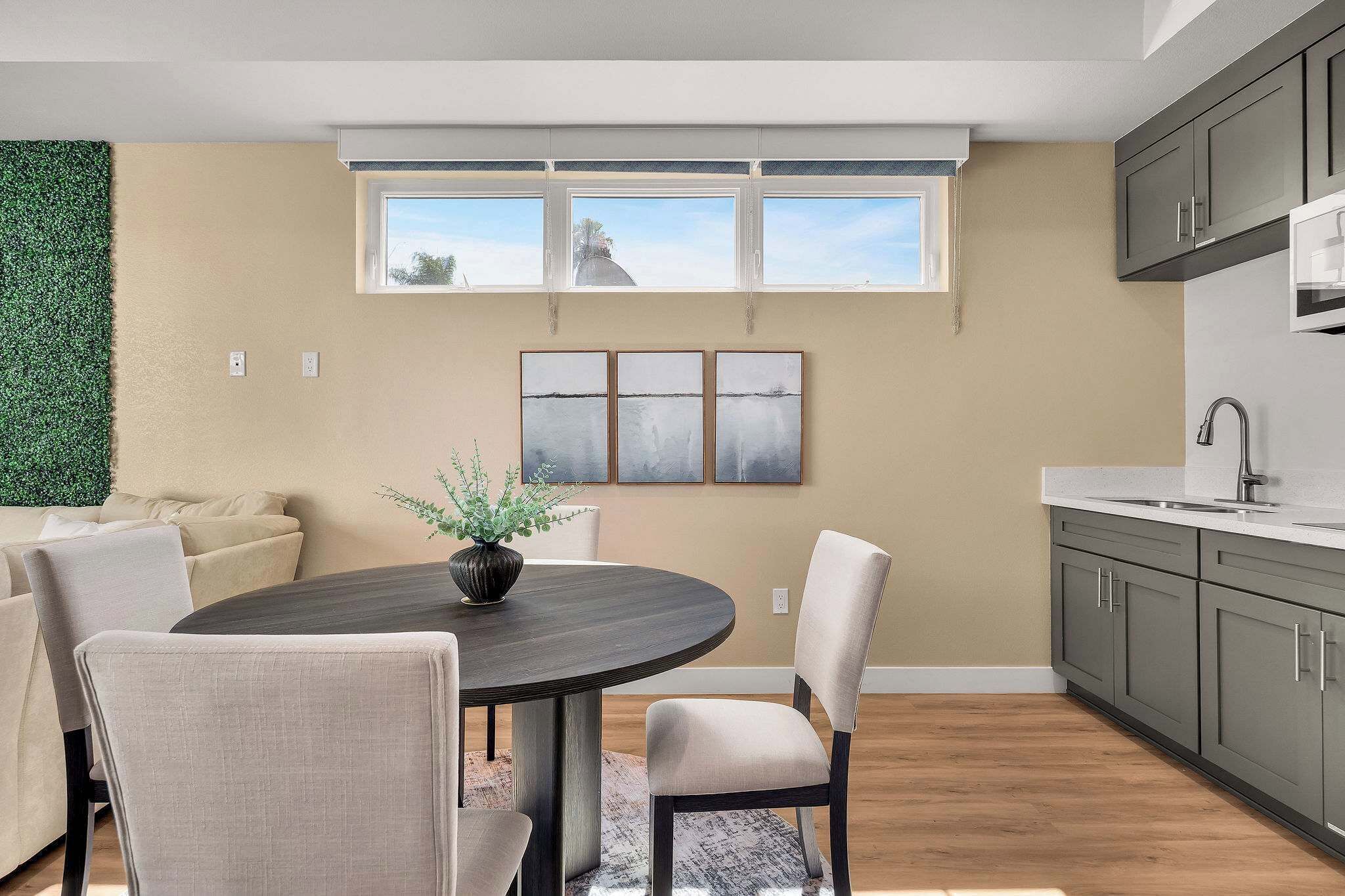 A modern kitchen with a dining area, large windows, and a view of the outdoors.