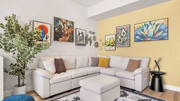 Una sala de estar moderna con un sofá modular blanco, una planta grande en maceta y varias obras de arte en la pared.