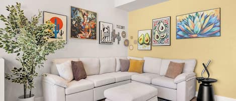 Una sala de estar moderna con un sofá modular blanco, una planta grande en maceta y varias obras de arte en la pared.