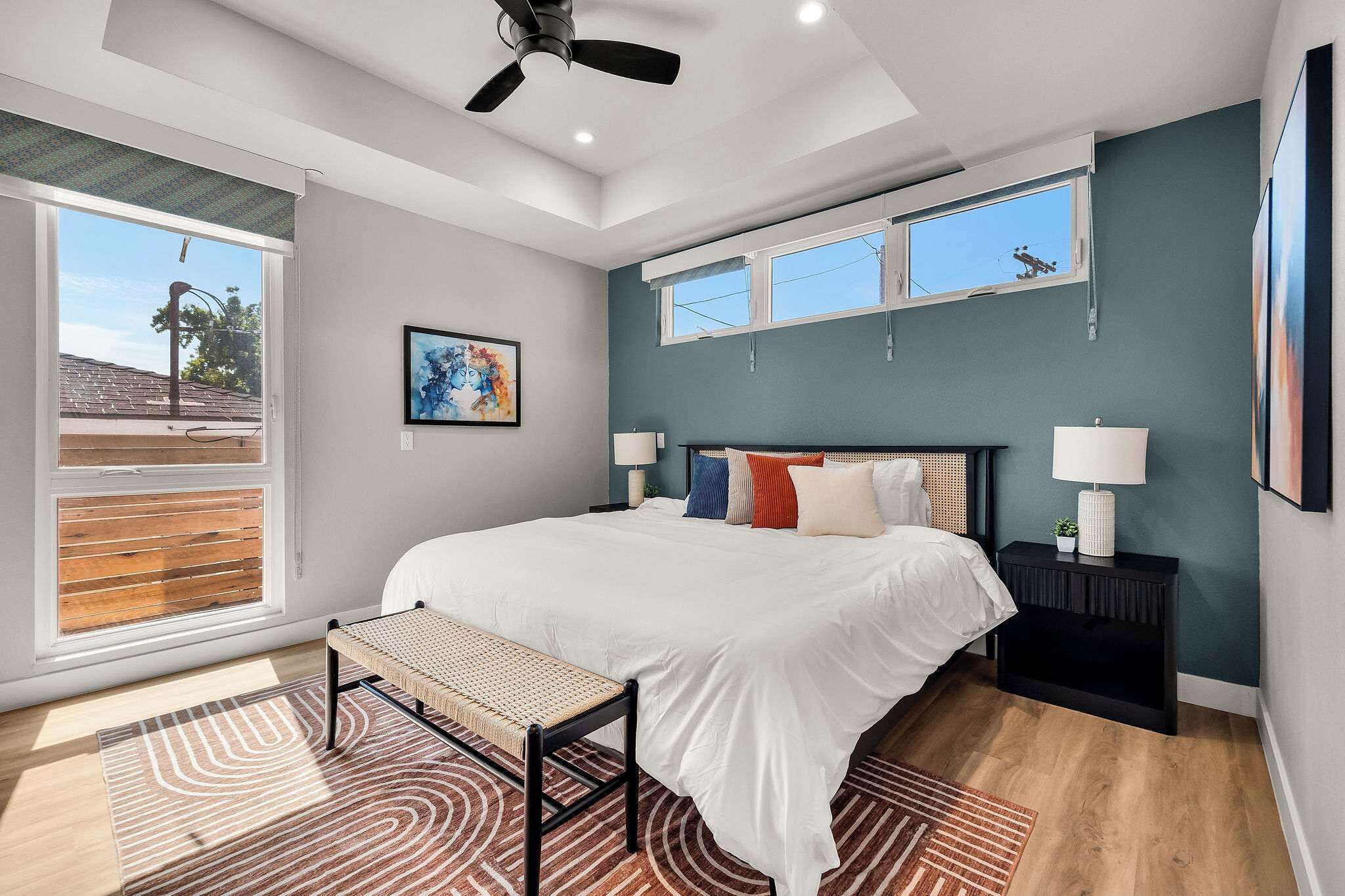 A modern bedroom with a large bed, a ceiling fan, two windows, and a view of the outside.