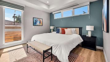 A modern bedroom with a large bed, a ceiling fan, two windows, and a view of the outside.