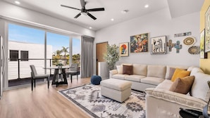 A modern living room with a sofa, a coffee table, a dining area with chairs, and a large window.