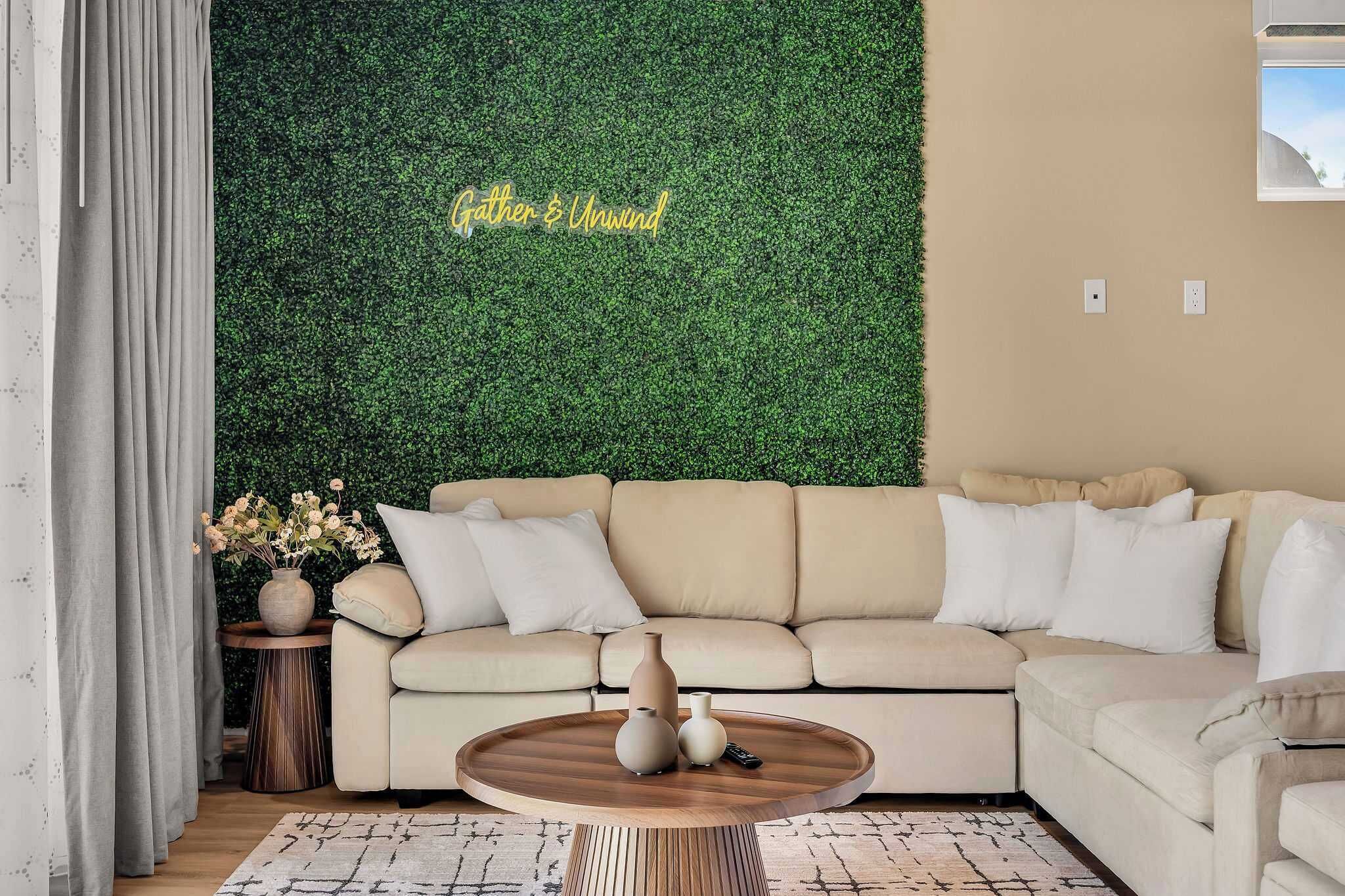A living room with a green wall, a beige sofa, a round wooden coffee table, and a small side table with a vase.