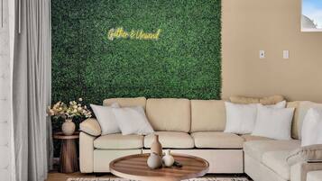 A living room with a green wall, a beige sofa, a round wooden coffee table, and a small side table with a vase.
