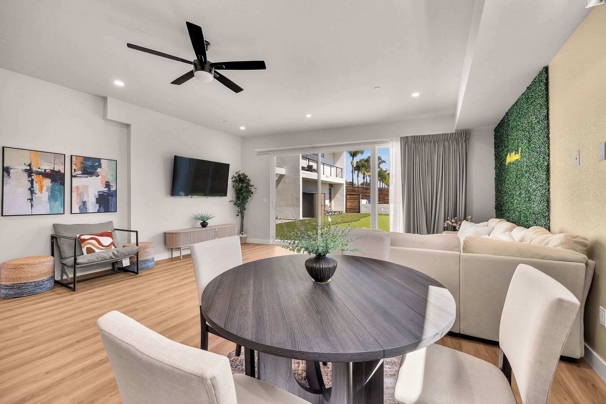A modern living room with a round dining table, a sofa, a flat-screen TV, and a ceiling fan.