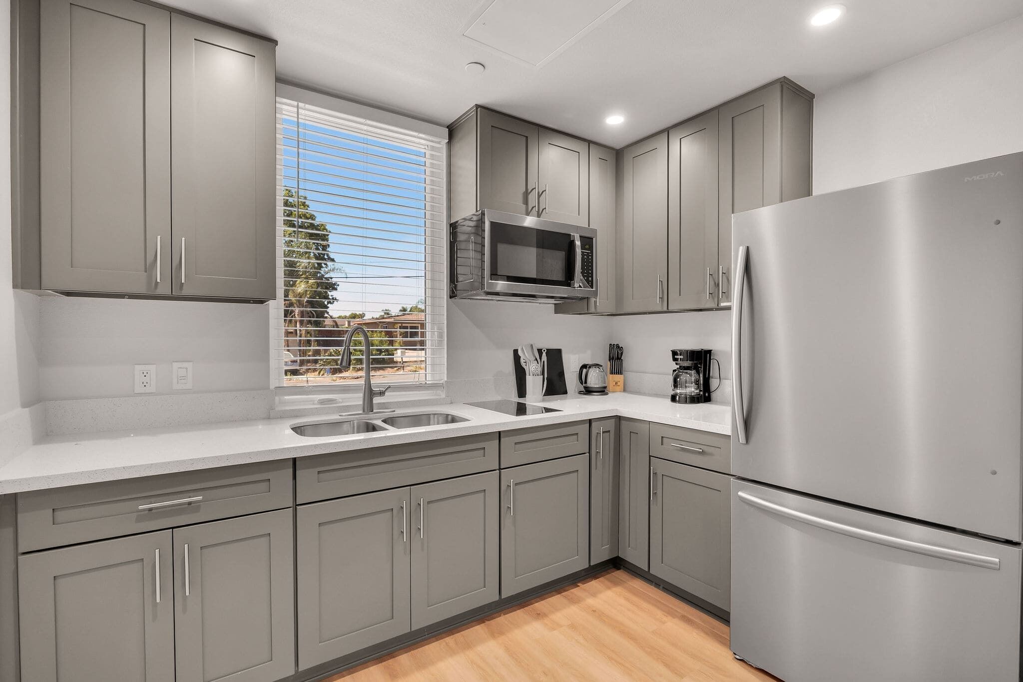 A modern kitchen with grey cabinets, stainless steel appliances, and a window with blinds.