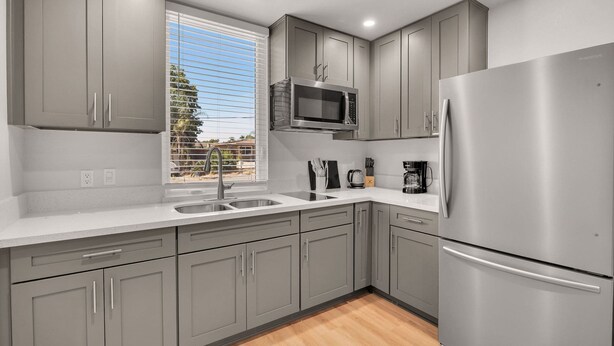 A modern kitchen with grey cabinets, stainless steel appliances, and a window with blinds.