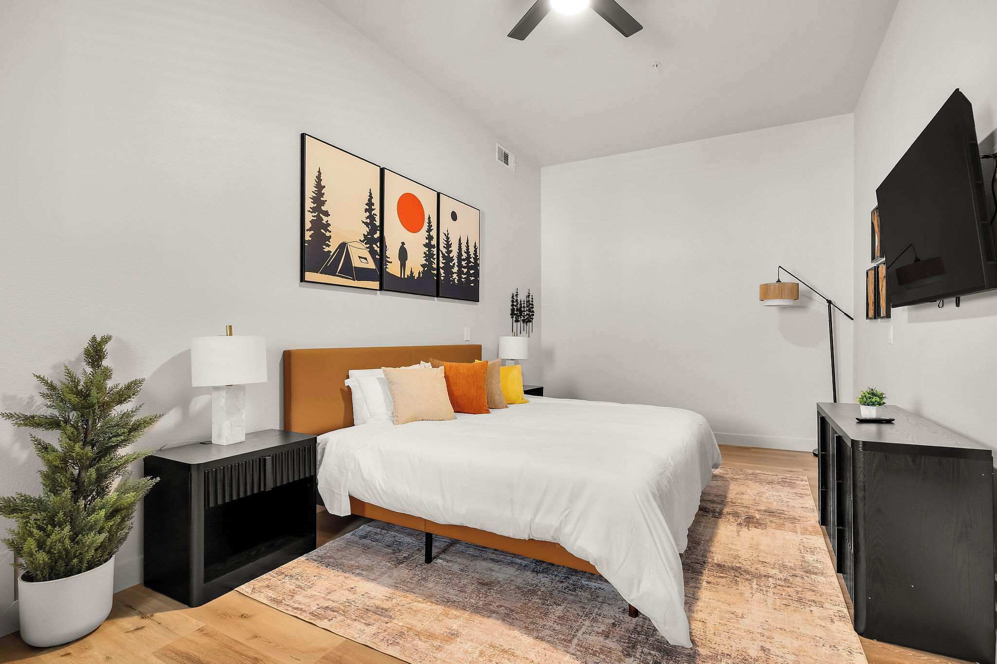 Un dormitorio moderno con cama, mesitas de noche, televisor y una obra de arte en la pared.