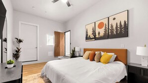 A modern bedroom with a large bed, a wooden headboard, and a view of the outdoors through a sliding door.