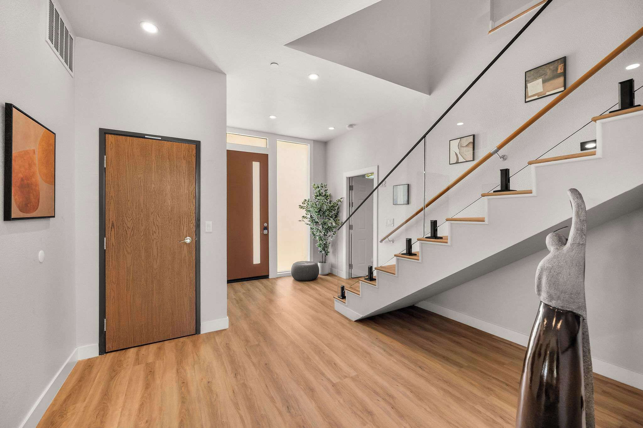 A modern interior with a wooden floor, a staircase with glass railings, and a door with a wooden finish.