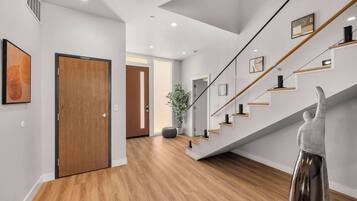 A modern interior with a wooden floor, a staircase with glass railings, and a door with a wooden finish.