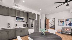 A modern kitchen with grey cabinets, a microwave, a refrigerator, and a dining area with a round table and chairs.