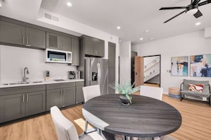 Una cocina moderna con armarios grises, microondas, refrigerador y comedor con mesa redonda y sillas.