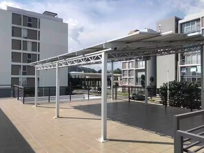 An outdoor area with a covered seating area, a building with multiple floors, and a clear sky. - Departamento de Lujo Exclusivo, Vista y Literas. (tlajomulco de zuñiga)