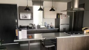 A modern kitchen with a central island, stainless steel appliances, pendant lighting, and a dark door. - Departamento de Lujo Exclusivo, Vista y Literas. (tlajomulco de zuñiga)