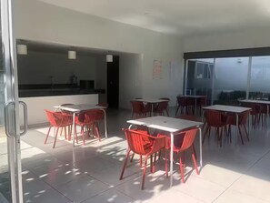 Un espace de restauration moderne avec des tables blanches et des chaises rouges, de grandes fenêtres et une vue sur la ville.