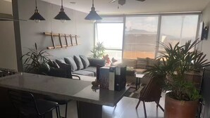 A modern kitchen with a central island, bar stools, and a dining area with a sofa and table. - Departamento de Lujo Exclusivo, Vista y Literas. (tlajomulco de zuñiga)