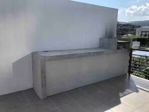 Eine Betonbank auf einem gefliesten Balkon mit weißer Wand und Metallgeländer.
