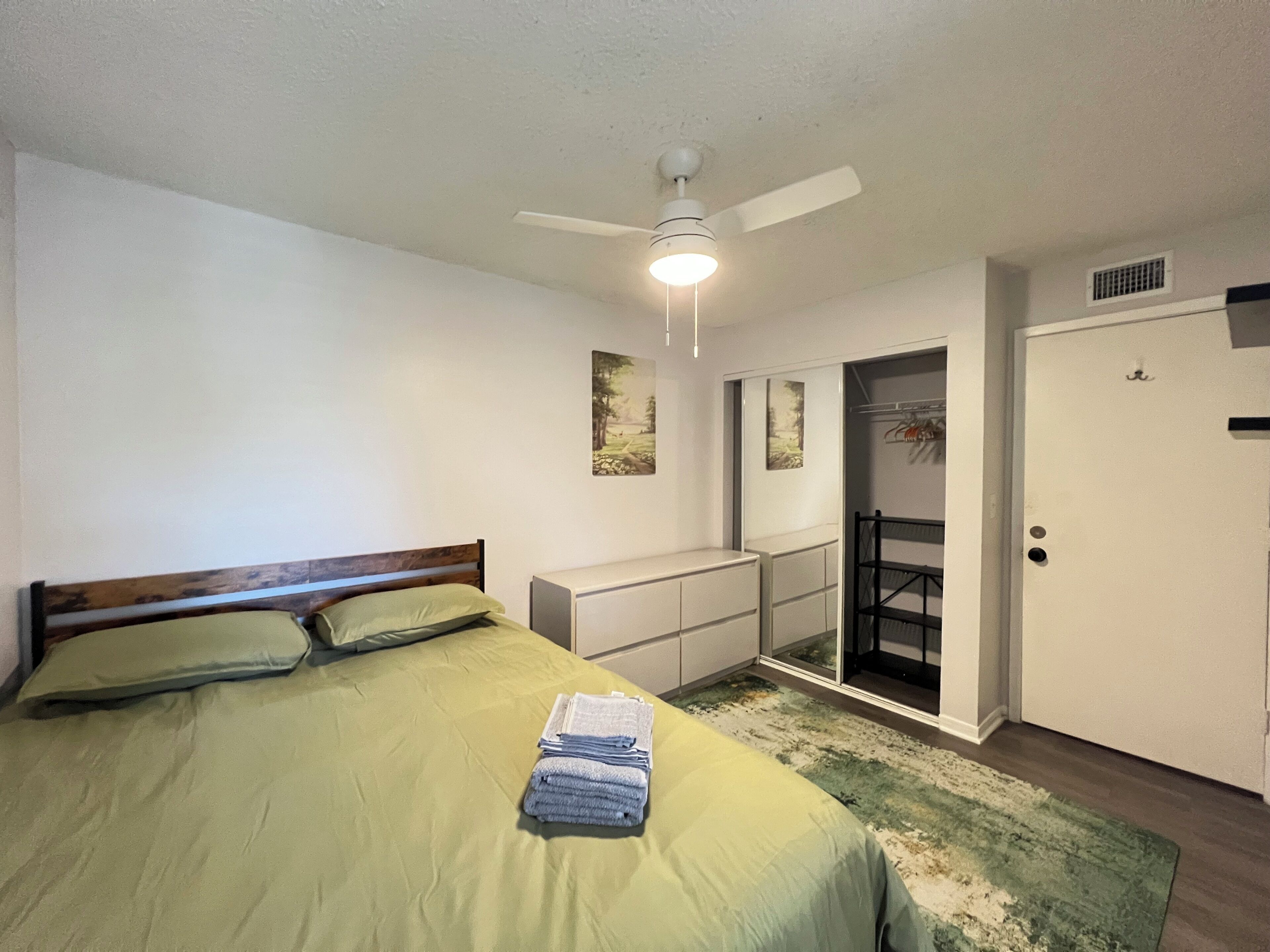 Une chambre à coucher avec un lit, un ventilateur de plafond, une porte et une petite fenêtre.
