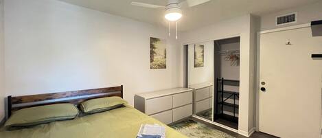 Une chambre à coucher avec un lit, un ventilateur de plafond, une porte et une petite fenêtre.