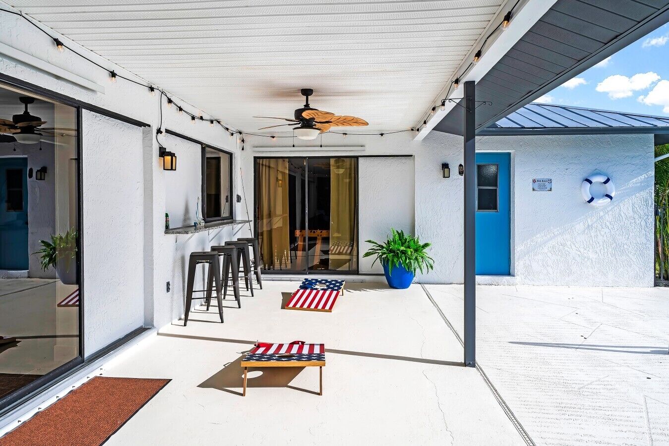 Un patio techado con ventilador de techo, asientos exteriores y una puerta azul.