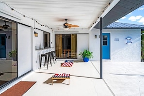 A covered patio with a ceiling fan, outdoor seating, and a blue door.
