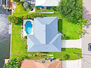 An aerial view of a house with a swimming pool, a large lawn, and a road nearby.