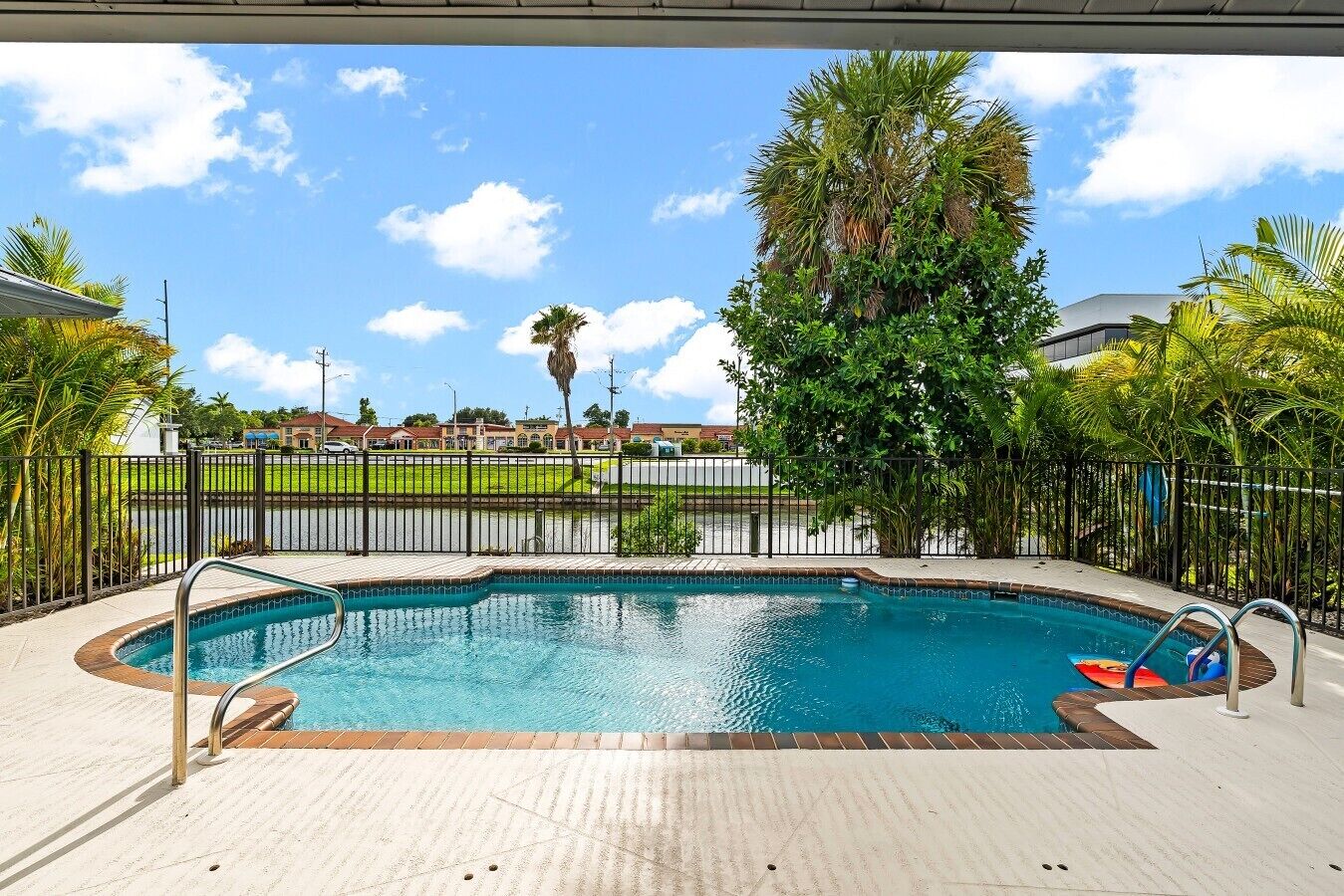 A swimming pool with a tiled deck, surrounded by a fence and palm trees.