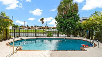 A swimming pool with a tiled deck, surrounded by a fence and palm trees.