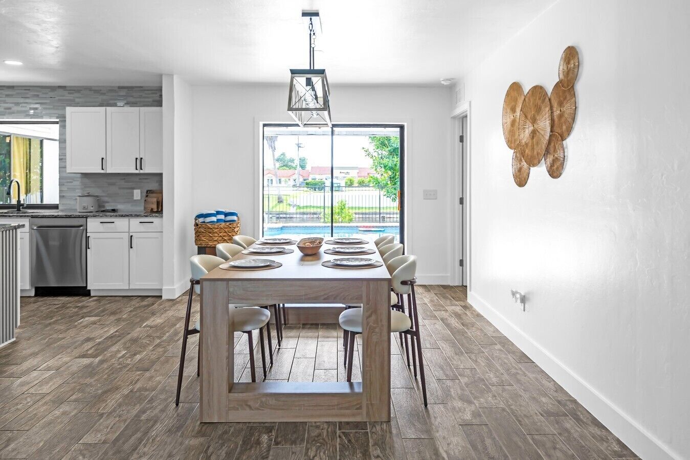 Eine moderne Küche mit weißen Schränken, ein Essbereich mit einem Holztisch, gedeckt für sechs Personen, und ein großes Fenster mit Blick auf eine Wohngegend.
