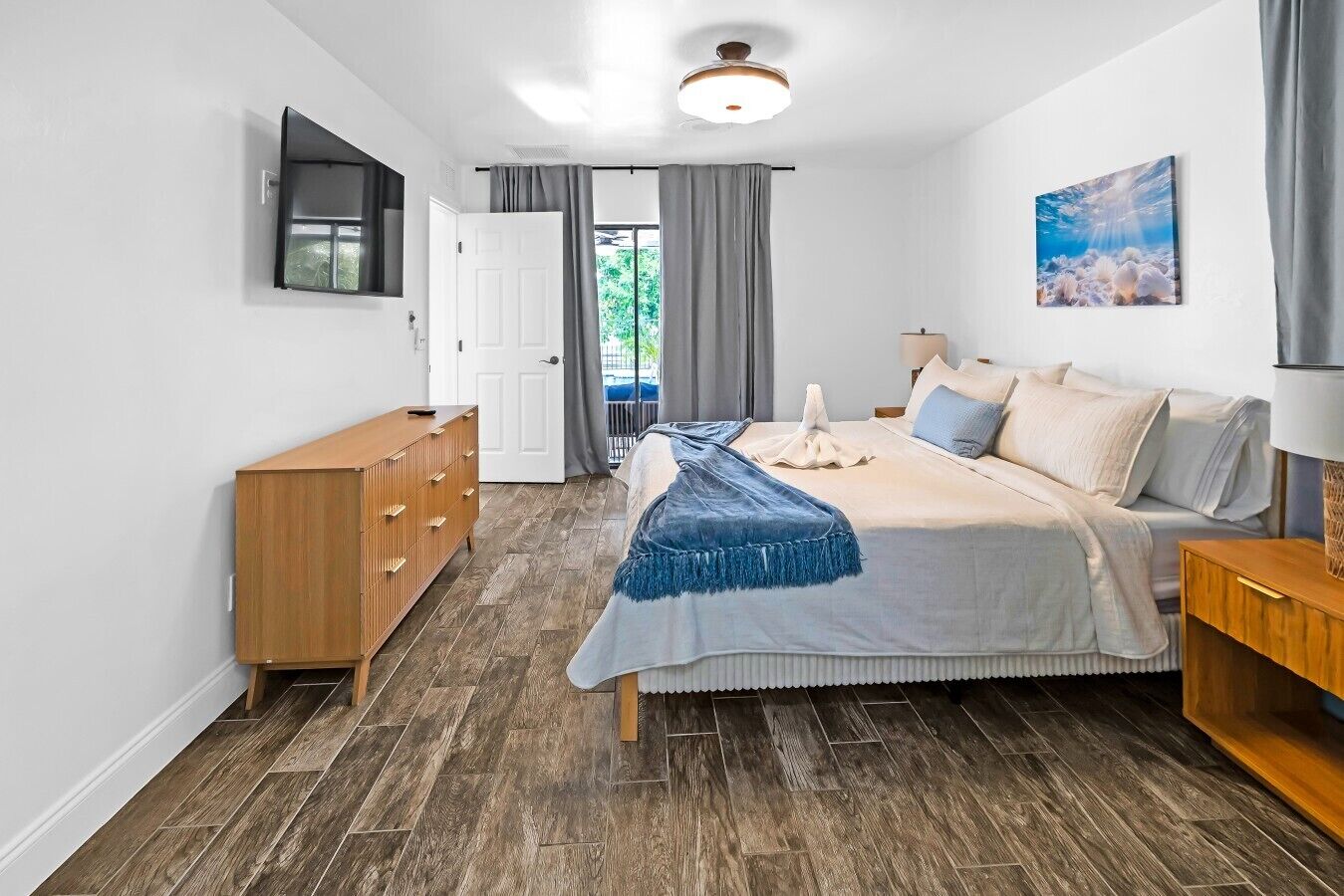 Un dormitorio con cama, cómoda, televisor, puerta y ventana con cortinas.