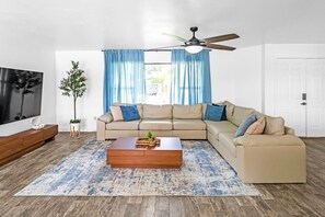 A living room with a sectional sofa, a coffee table, a TV, and a ceiling fan.
