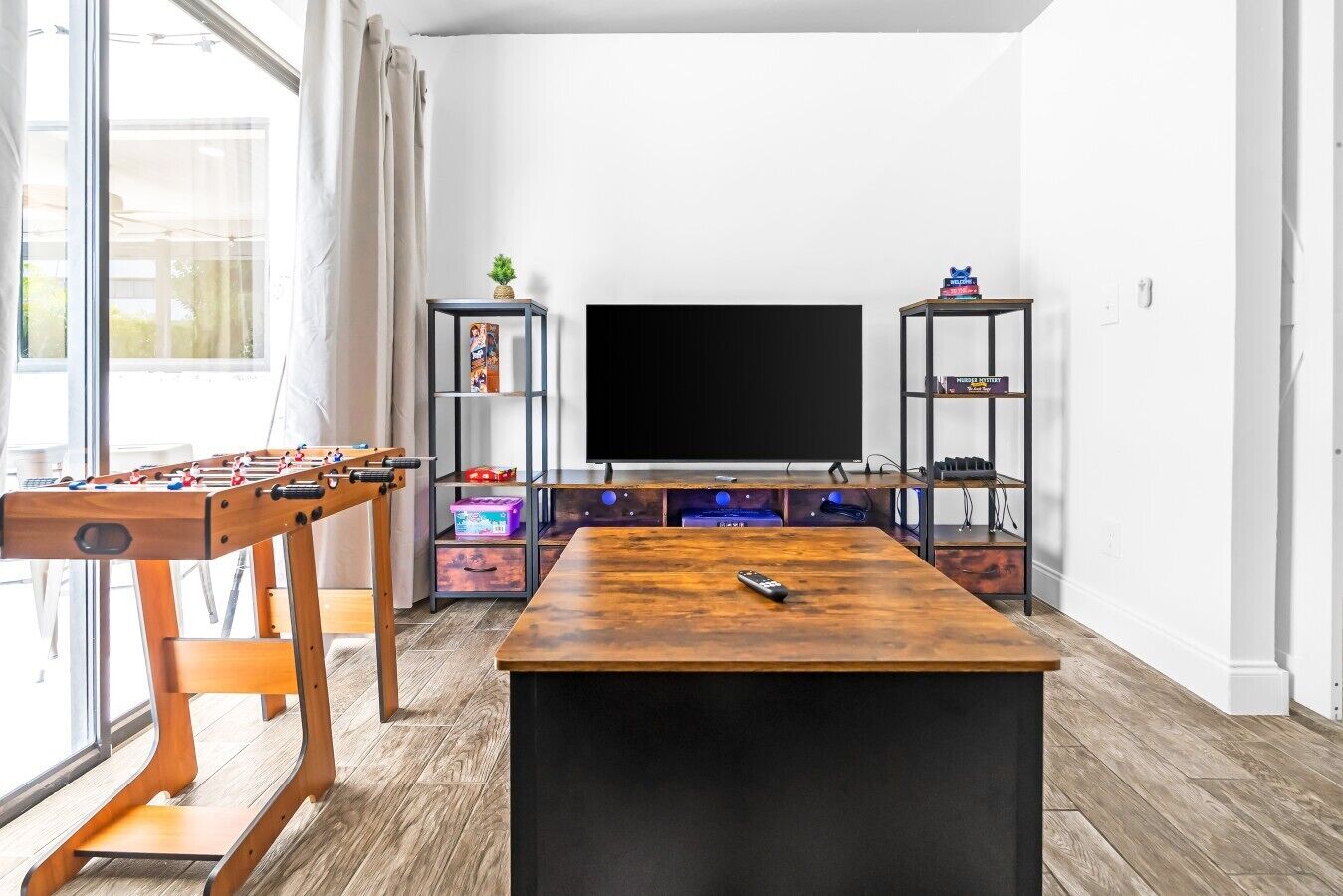 A living room with a foosball table, a flat-screen TV, and shelves with books and decorative items.