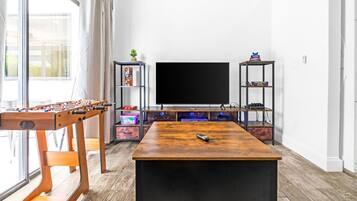 A living room with a foosball table, a flat-screen TV, and shelves with books and decorative items.