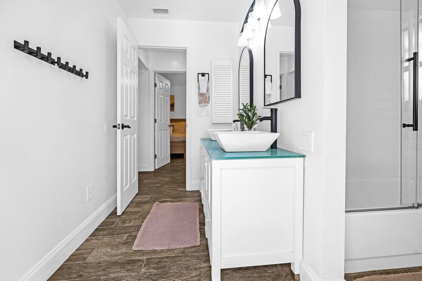 Un pasillo que conduce a un baño con un lavabo blanco, un espejo y una ducha.