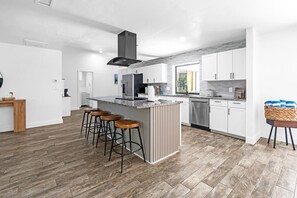 A modern kitchen with a central island, bar stools, white cabinetry, and a dishwasher.