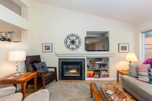 Ein Wohnzimmer mit Kamin, Fernseher, Bücherregal und einer Couch.