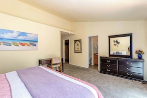 Ein Schlafzimmer mit einem Bett, einem Schminktisch, einem Stuhl, einem Bild von Booten und einer Tür zu einem anderen Raum.