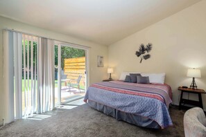 Ein Schlafzimmer mit einem Bett, einem Nachttisch, einer Lampe, einem Sessel und einer Glastür, die auf eine Terrasse führt.