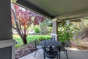 Une terrasse couverte avec une table et des chaises, un arbre aux feuilles rouges et une cour gazonnée.