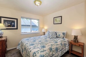 Ein Schlafzimmer mit einem Bett, zwei Nachttischlampen, einem Fenster und zwei gerahmten Bildern an der Wand.