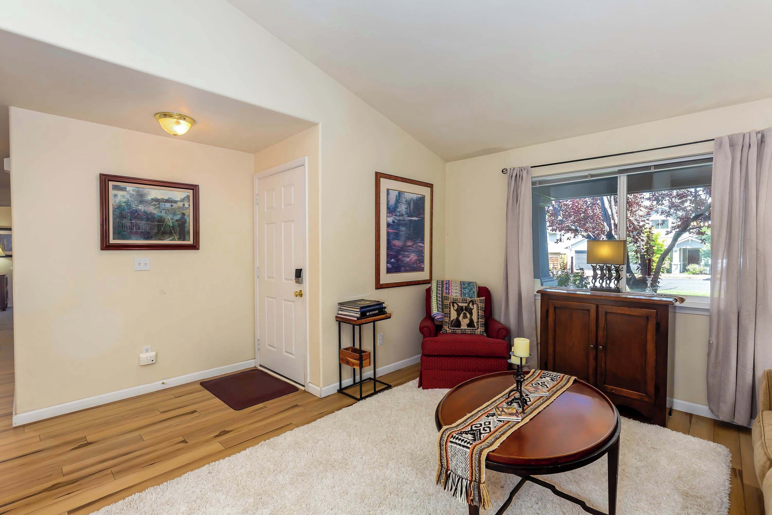 A room with a wooden floor, a white rug, a red armchair, a table with a blanket, and two framed pictures on the wall.