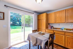 A dining area with a table set for two, wooden cabinets, and a sliding glass door leading to a backyard. - Near Old Mill: Dog-Friendly Bend House w/ BBQ and Fenced yard (Bend)