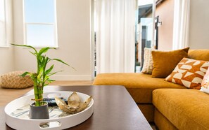 Uma sala de estar moderna com sofá, almofadas, uma mesa de centro, uma planta decorativa e uma bandeja com uma tigela e uma xícara.